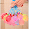 A hand is squeezing a cluster of blue water balloons, with many other colored balloons hanging down.