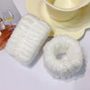 White microfiber wrist sweatband and scrunchies for face washing displayed on a light yellow plate.