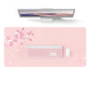 A pink waterproof PU leather desk pad featuring a white keyboard and mouse, with pink cherry blossoms in the background.