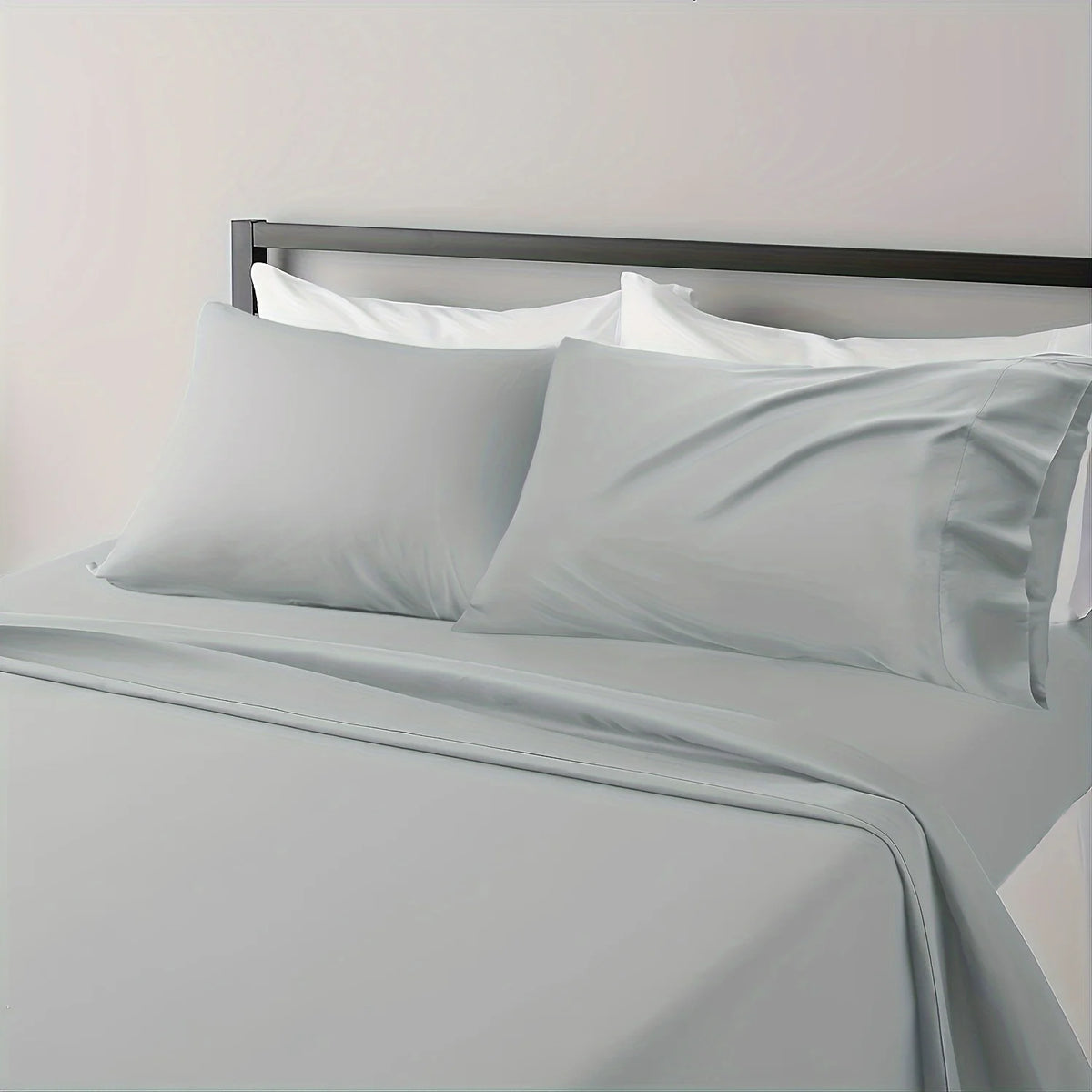 A close-up of a bed with white linens and a gray duvet, featuring a modern metal headboard.
