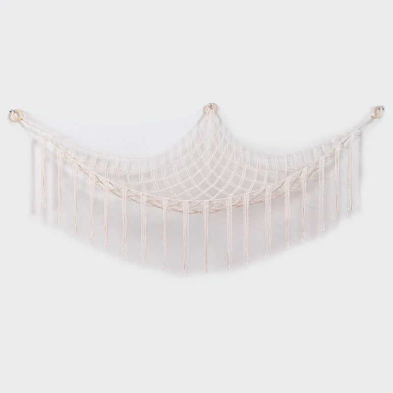 A cream-colored bohemian plush toy storage hammock with fringe details.