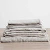 A stack of light gray pure linen bed sheets and pillowcases folded neatly on a wooden surface.