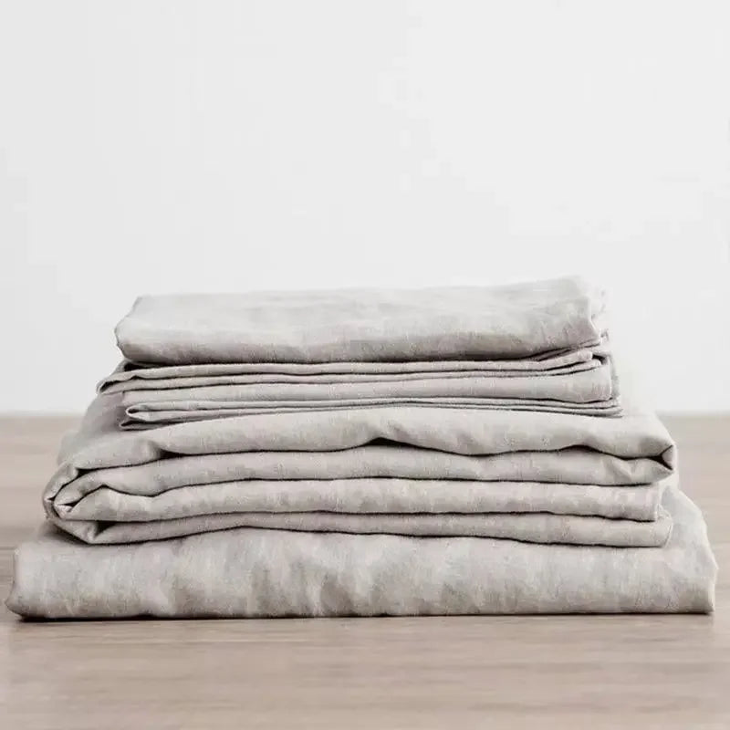 A stack of light gray pure linen bed sheets and pillowcases folded neatly on a wooden surface.