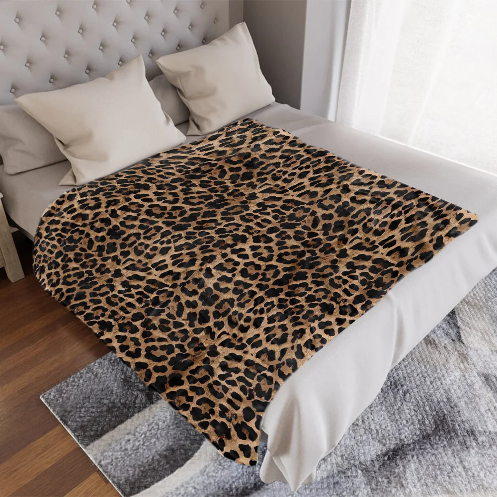 A leopard print flannel throw blanket draped over a white duvet on a bed.