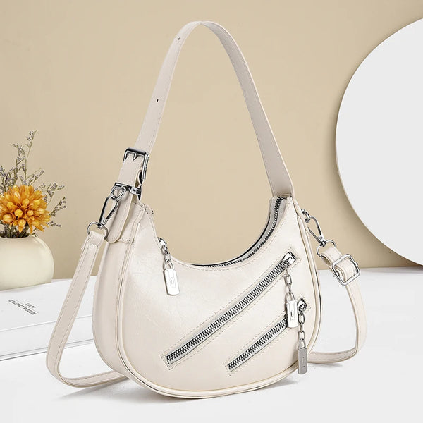 Bolso cruz de cuero sintético beige estilo vintage con cremallera y herrajes plateados sobre una superficie blanca.