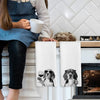 A set of two white kitchen towels featuring illustrations of dogs and glasses