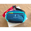 A blue waterproof nylon fanny pack with a red strap and black accents resting on a white box.