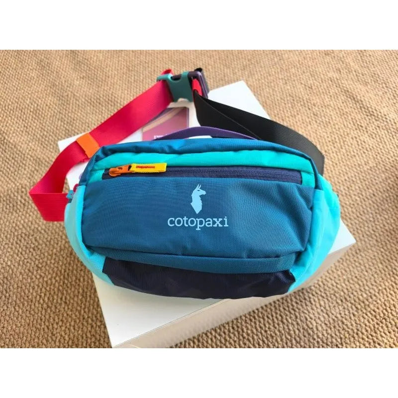 A blue waterproof nylon fanny pack with a red strap and black accents resting on a white box.