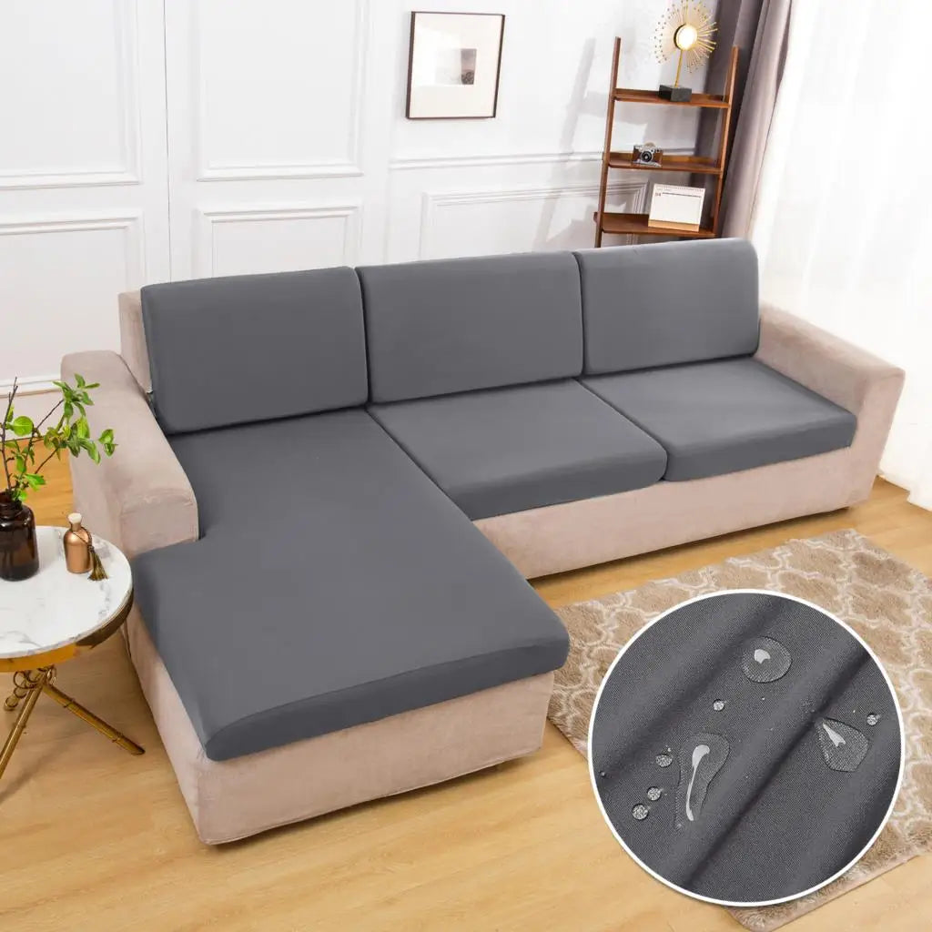 A gray waterproof sofa cushion cover with an elastic edge is displayed on a light-colored sofa.