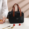 A black thermal lunch tote bag with brown straps is shown next to a white shirt and cutlery on a table.