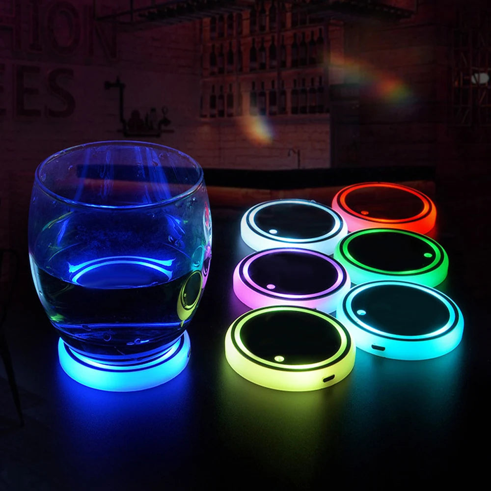 A glass filled with blue liquid sits next to several circular LED lights displaying various colors on a dark surface.