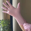 Eine Hand trägt eine rosa Einweg-Nitril-Haube für die Küche vor einem unscharfen Hintergrund.