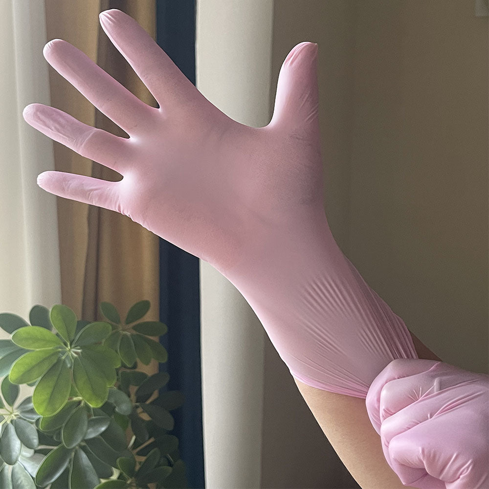 Eine Hand trägt eine rosa Einweg-Nitril-Haube für die Küche vor einem unscharfen Hintergrund.