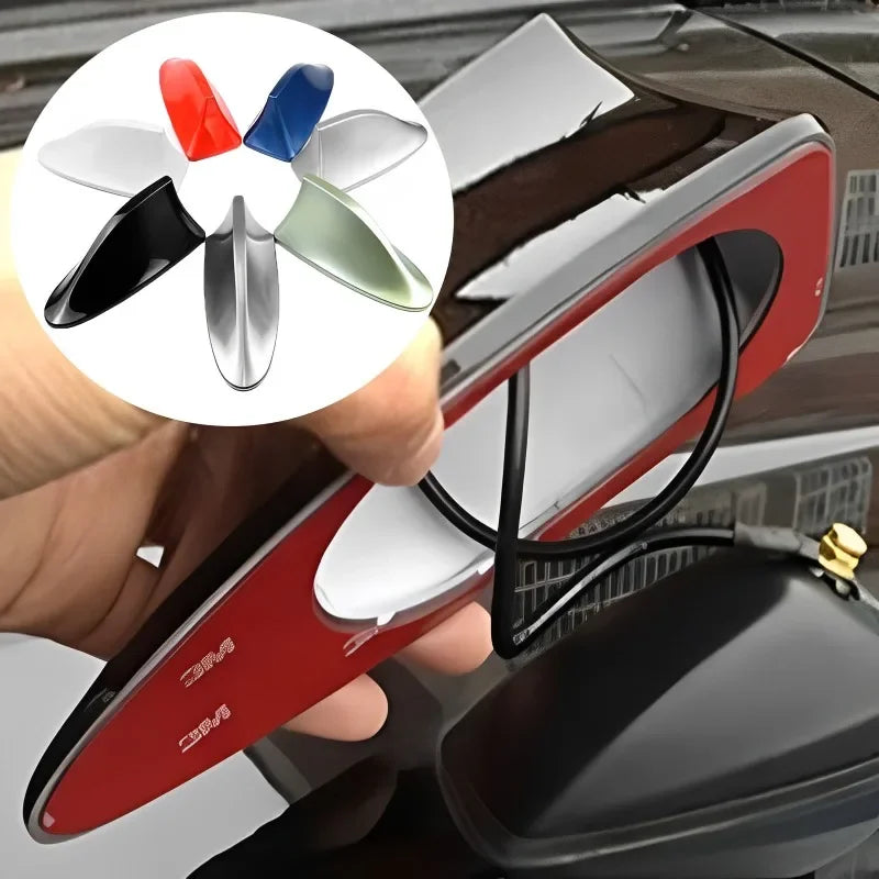 A hand holds a red car antenna with a fin design, showing various color options for FM/AM signal enhancement.