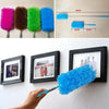 A hand is holding a bright blue electrostatic telescopic dust duster with a flexible stainless steel handle against a white b
