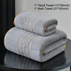 A stack of gray hand towels and a bath towel with gold accents displayed on a dark surface.