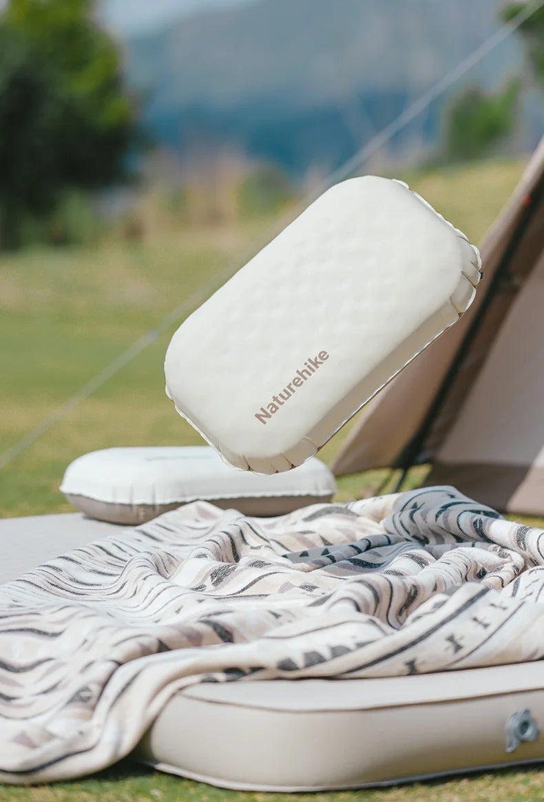 A white Naturehike foam inflatable camping pillow resting on a tan mat outdoors.