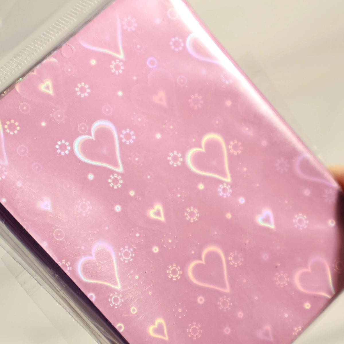 A close-up of holographic pink heart-shaped card sleeves with sparkling accents.