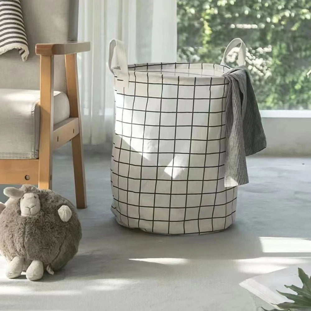 A large, white and black checkered laundry basket with handles sits on a light gray floor next to a wooden chair and a sheep.