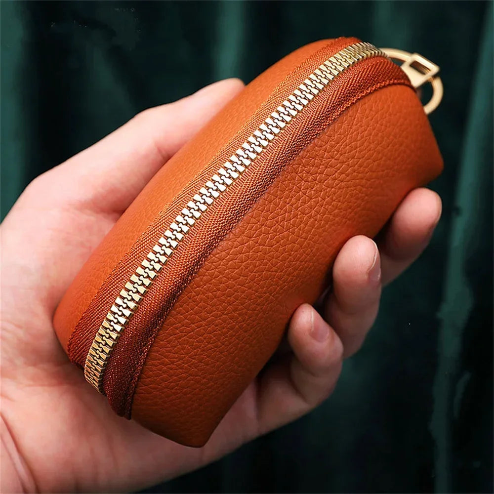 A hand holds an orange PU leather key organizer wallet with a visible zipper and gold clasp.