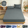 A fitted bed sheet in solid gray fabric is displayed on a wooden bed frame with a headboard and decorative mirror.