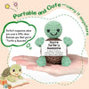 A handmade crochet turtle doll with a positive message card is held in a person's hand.