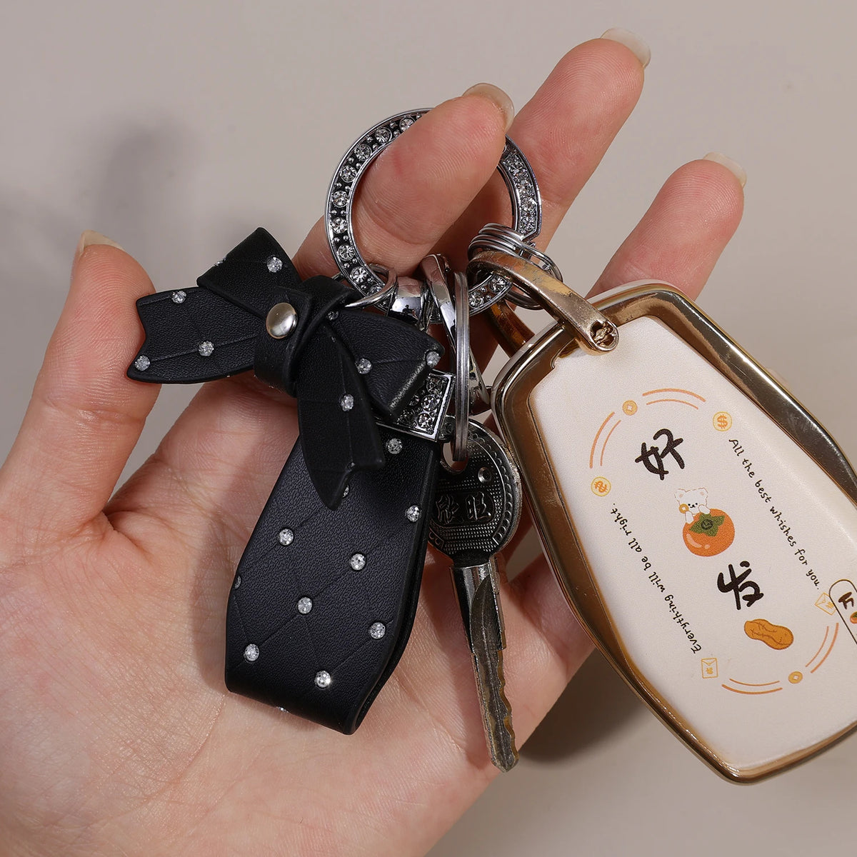 A hand holds a black PU leather bow keychain with an O-shaped silver buckle and a rectangular tag.