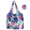 A white fabric tote bag featuring a vibrant tropical floral pattern in shades of purple, pink, and green.
