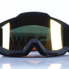 A pair of black retro motorcycle sunglasses with night vision lenses resting on a reflective surface.