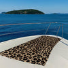 A leopard print towel laid out on the deck of a boat overlooking the sea and a distant island.