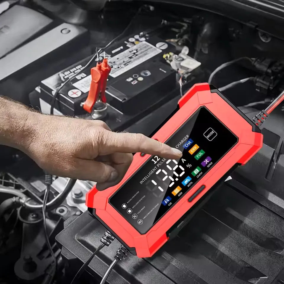 A hand points at a red intelligent car battery charger with an LCD display, positioned on a black vehicle surface.