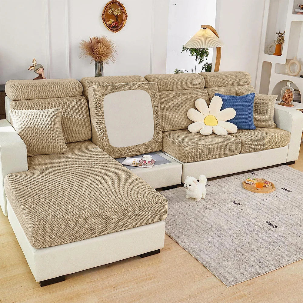 A beige jacquard elastic sofa slipcover with light gray fabric and white accents sits on a wooden floor.