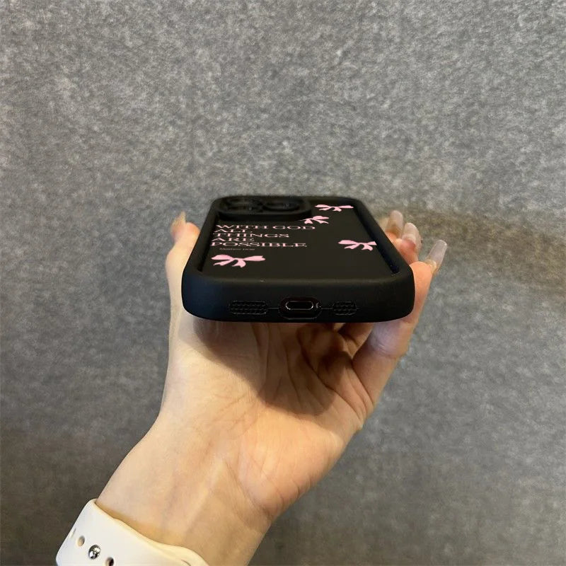 A hand holds a black silicone phone case with pink bow slogans on an iPhone.