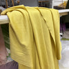 A drape of elegant yellow stretch jersey fabric is displayed on a wooden surface.