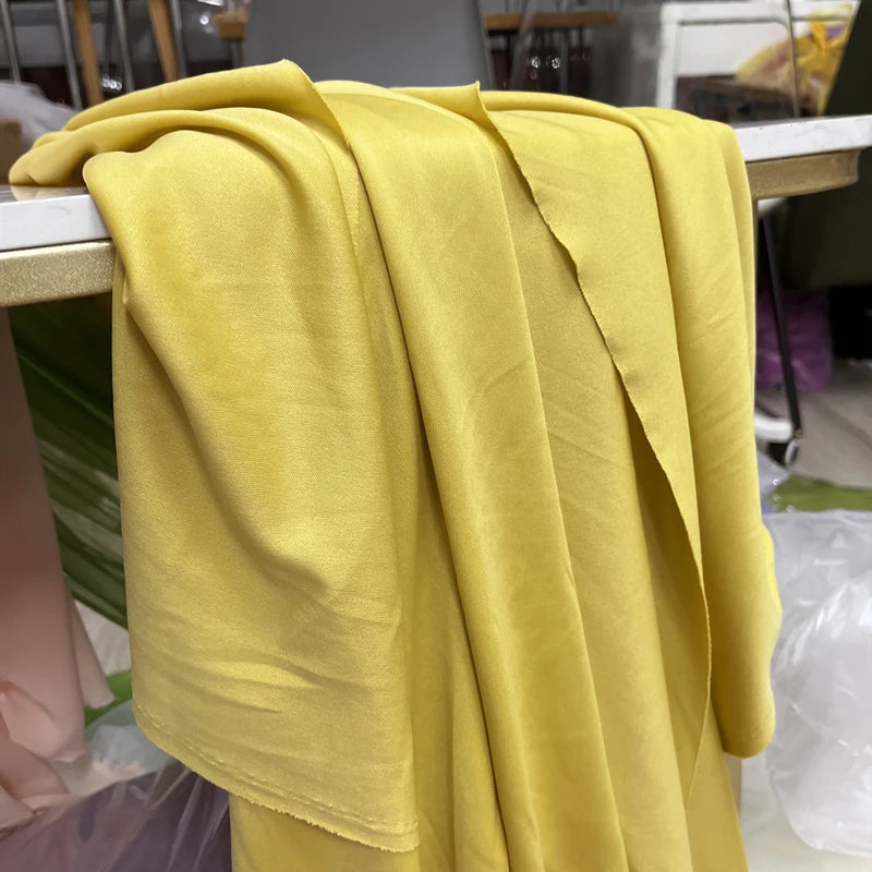 A drape of elegant yellow stretch jersey fabric is displayed on a wooden surface.