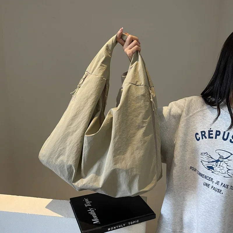 A light beige nylon tote bag is shown being held by a person against a neutral background.