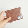A hand holds a brown genuine leather slim card holder wallet sealed in plastic.