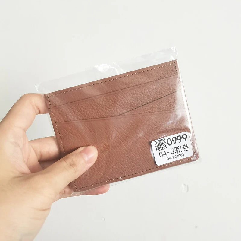A hand holds a brown genuine leather slim card holder wallet sealed in plastic.