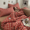 A close-up of a red and green plaid duvet cover set displayed on a bed with pillows and a teddy bear.