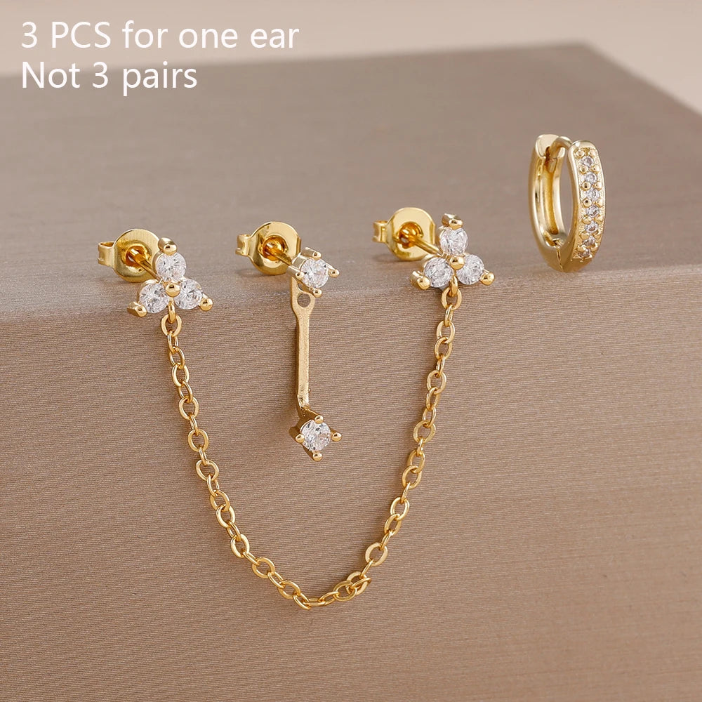 Boucles d'oreilles en chaîne dorée avec des accents zircon verts sur fond neutre.