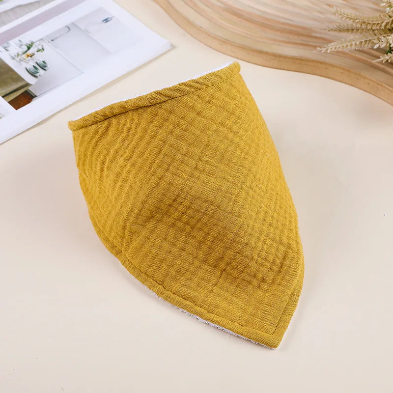 A mustard yellow soft cotton baby bib folded and lying on a light surface.