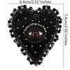 A black heart-shaped patch adorned with silver and black beads and a central eye design.