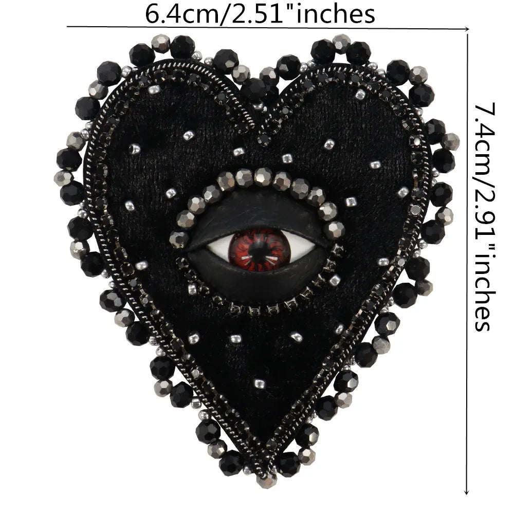 A black heart-shaped patch adorned with silver and black beads and a central eye design.