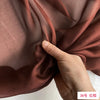 A hand is gently folding a piece of dusty rose colored silk chiffon fabric.