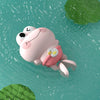 A pink cartoon turtle toy floating in blue water with green foliage visible.