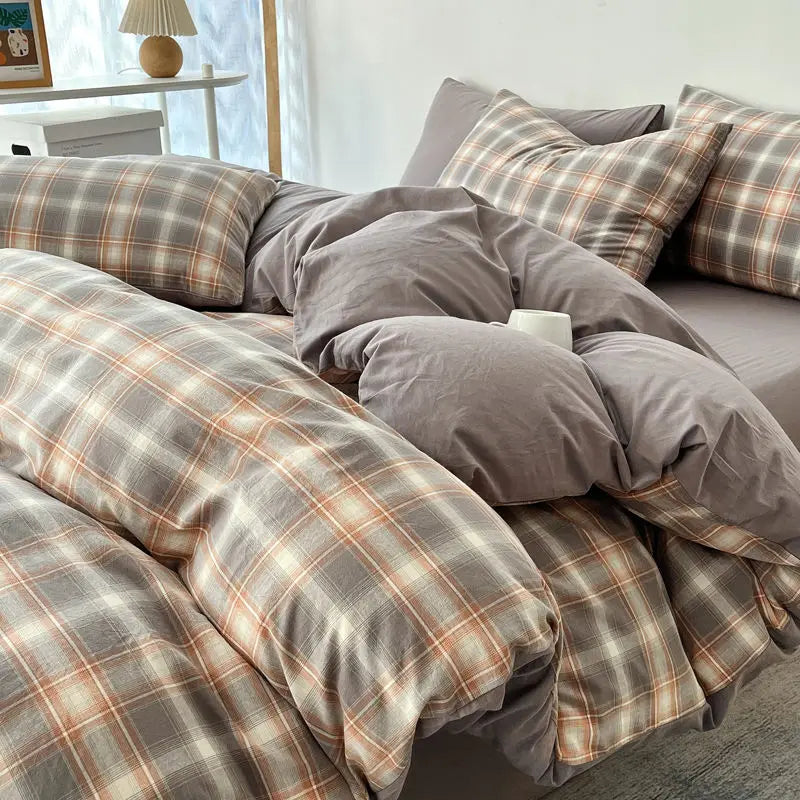 A close-up of a plaid bedding set featuring gray, brown, and orange tones on a bed.