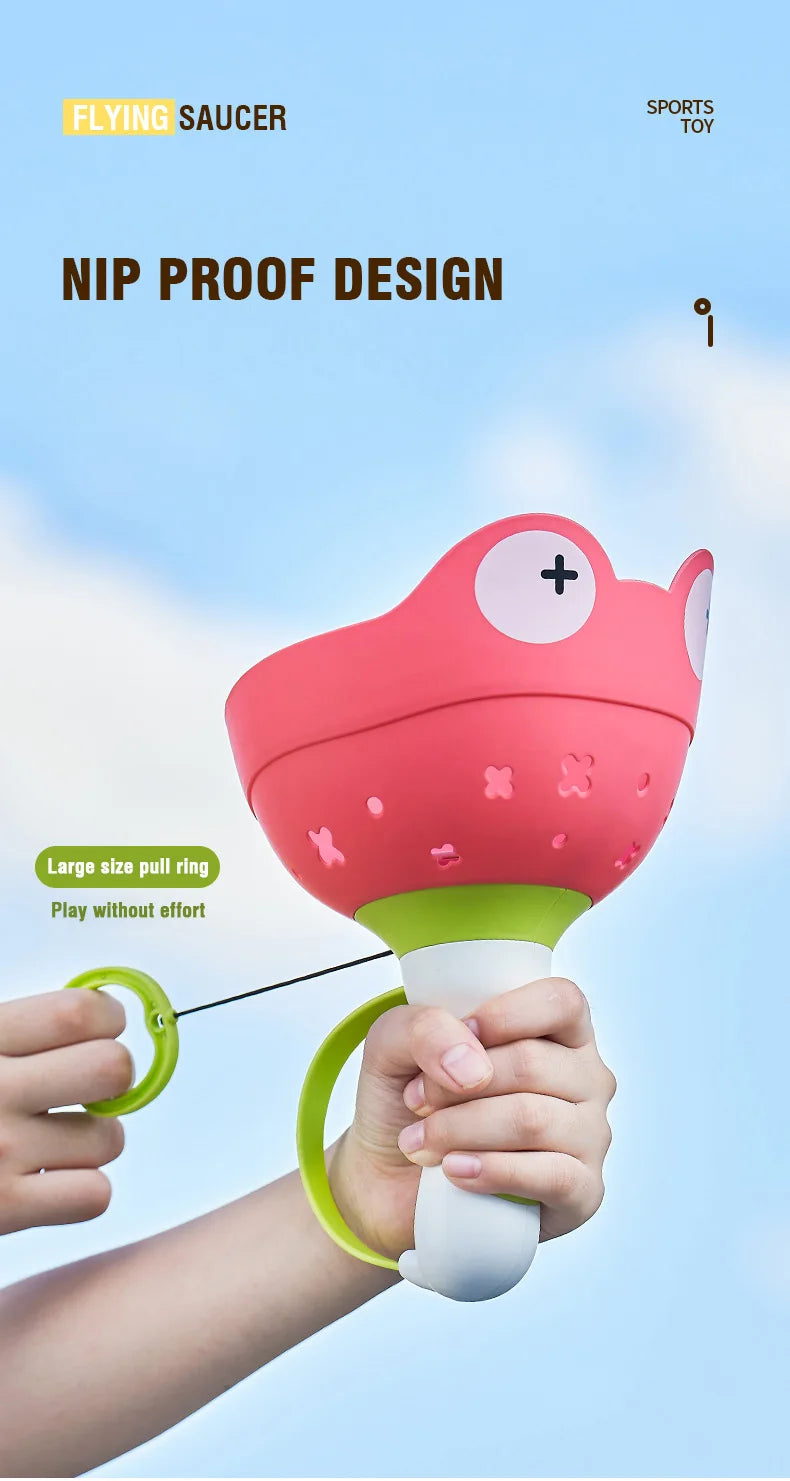 A hand is holding a pink flying saucer toy with a green pull ring, demonstrating its design.
