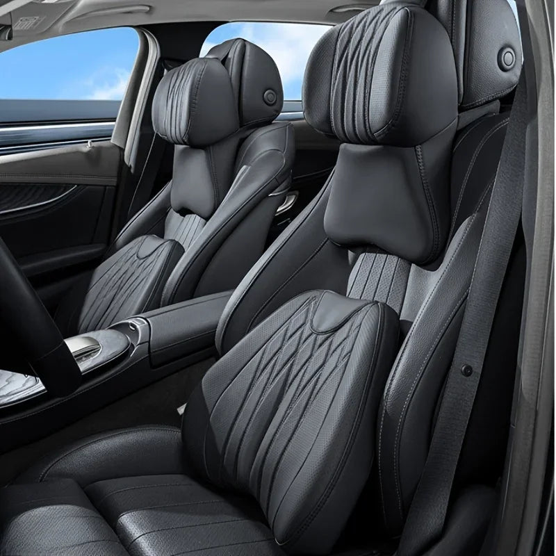 Interior view of a car seat showing memory foam lumbar support and neck pillows on black leather seats.