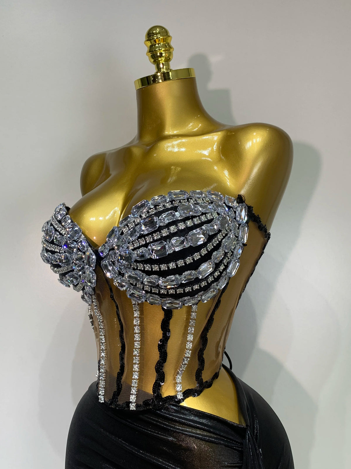 A gold mannequin displays a sparkly two-piece party outfit with a see-through top and black detailing.