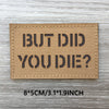 A rectangular tan woven patch with black text that reads BUT DID YOU DIE? on a gray wooden surface.